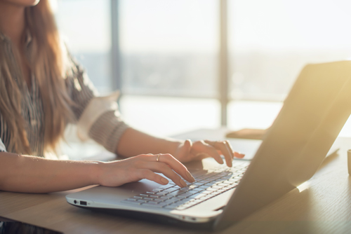 Geschäftsfrau sitzt am Schreibtisch in der Sonne und tippt auf ihrem Laptop