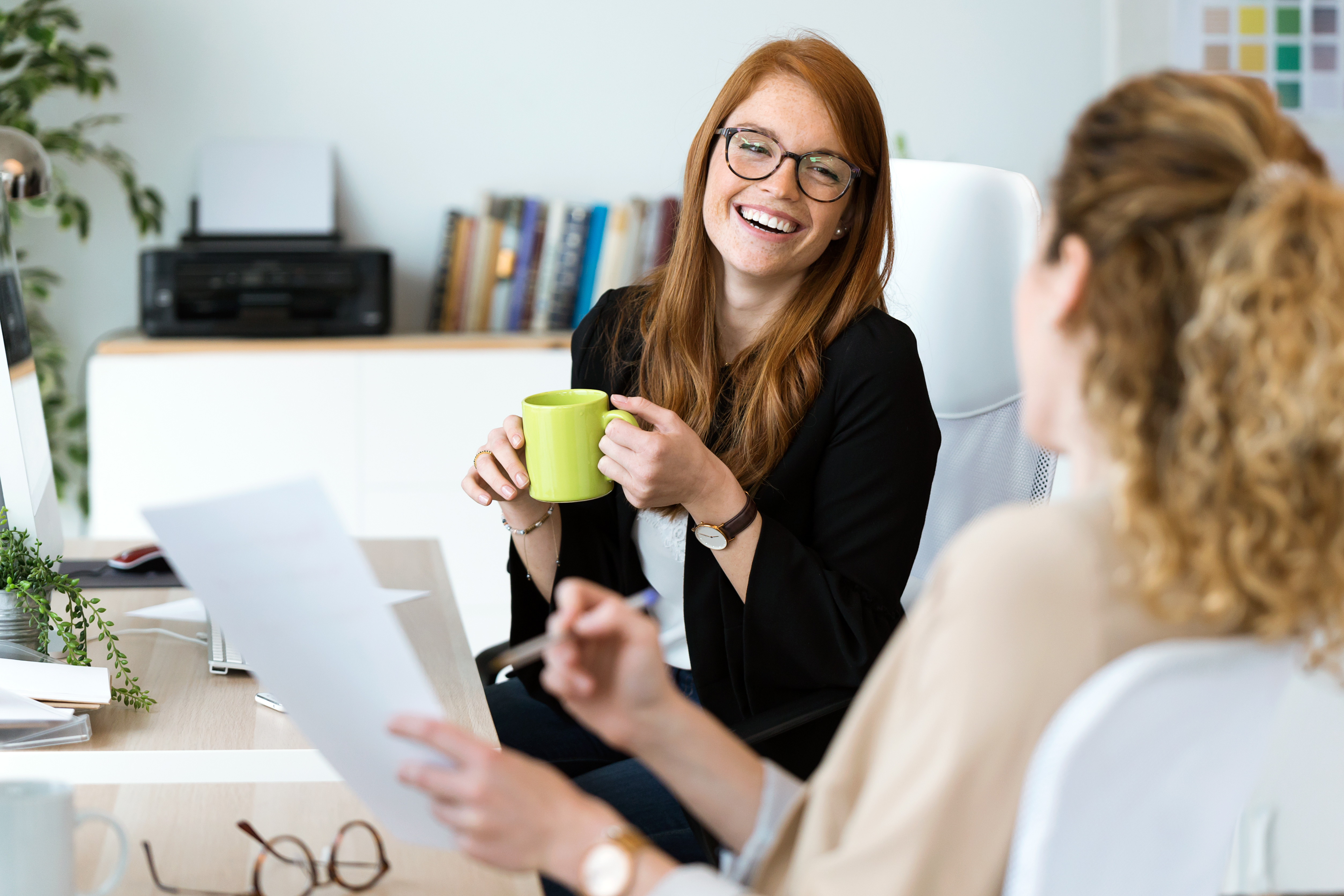 Zwei Frauen sitzen an einem Schreibtisch und unterhalten sich in gelöster Stimmung